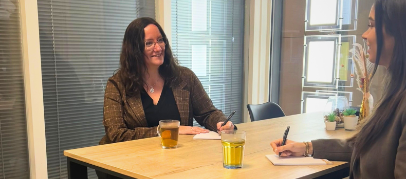 Vrouwelijke intercedent aan tafel met thee en kladblok in gesprek