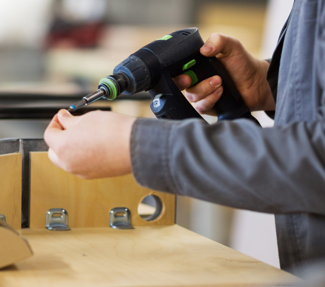Assemblagemedewerker gebruikt een elektrische schroefmachine om een schroef in een houten oppervlak te draaien