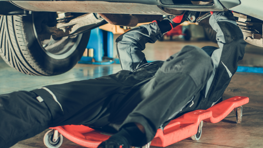 Automonteur die onder een auto aan het sleutelen is