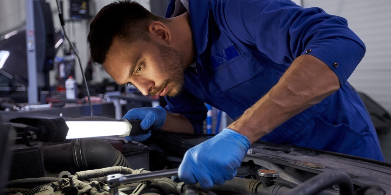 Automonteur die met een lamp en dopsleutel een auto inspecteert