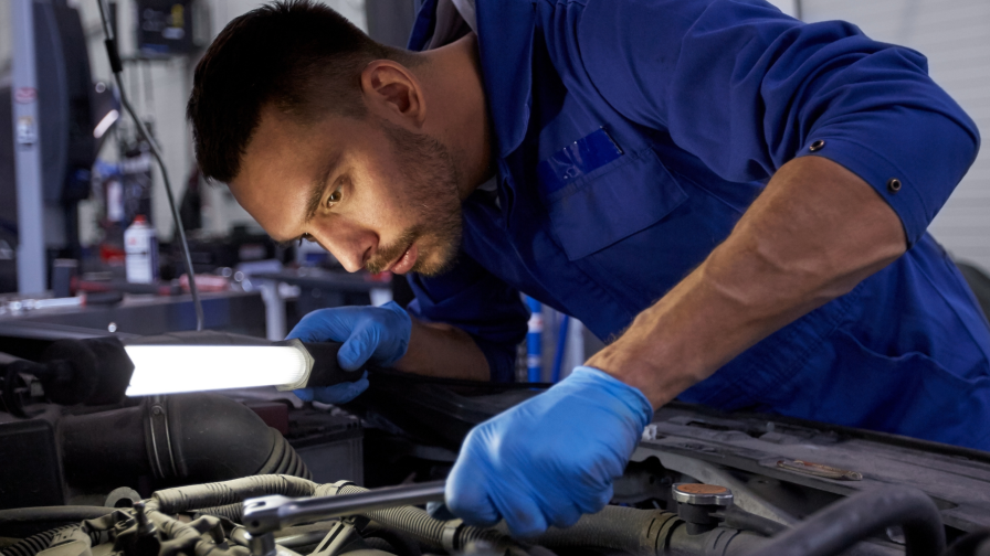 Automonteur die met een lamp en dopsleutel een auto inspecteert