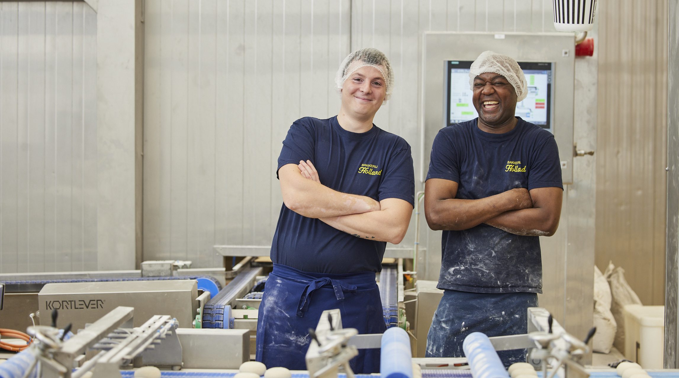 2 potige mannen die in een industriële bakkerij glimlachend hun werk doen