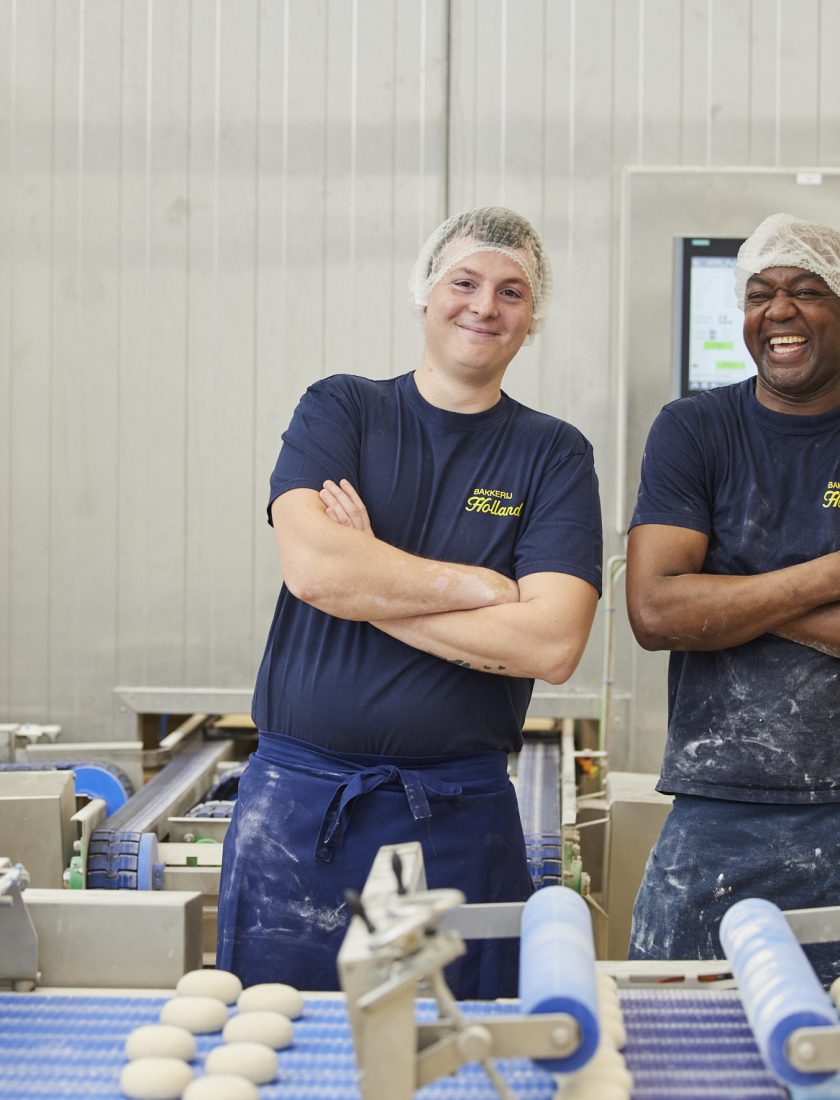 2 potige mannen die in een industriële bakkerij glimlachend hun werk doen