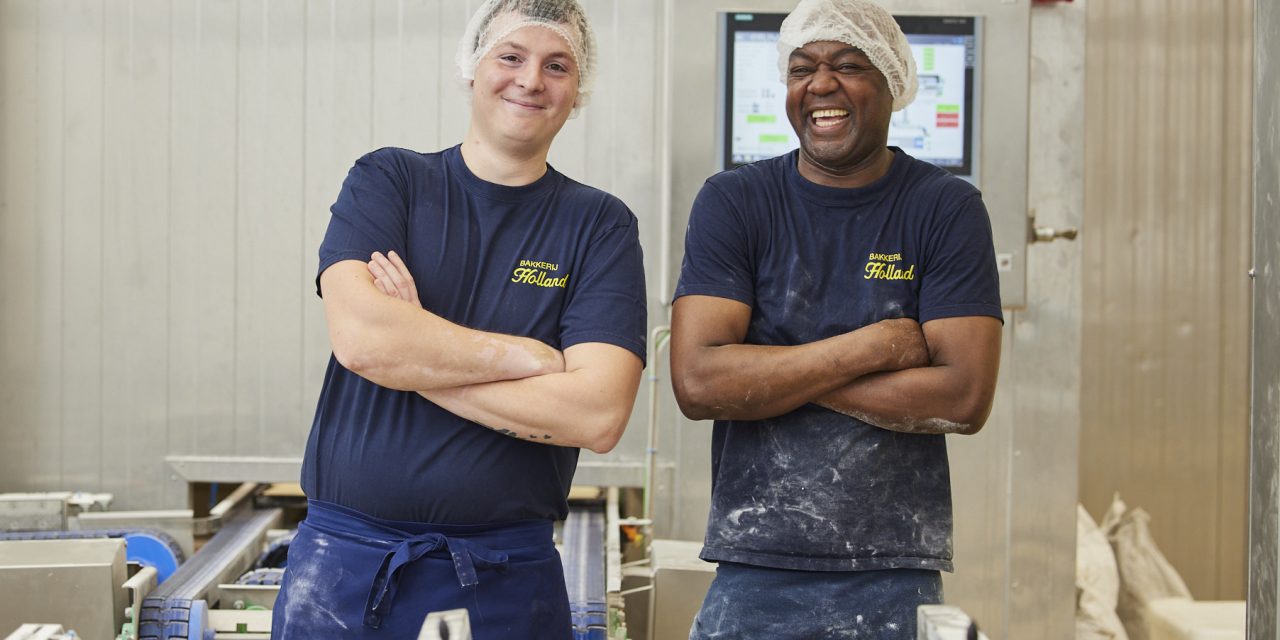 2 potige mannen die in een industriële bakkerij glimlachend hun werk doen