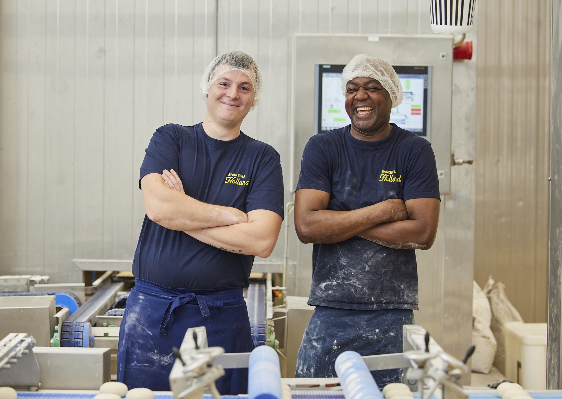 2 potige mannen die in een industriële bakkerij glimlachend hun werk doen