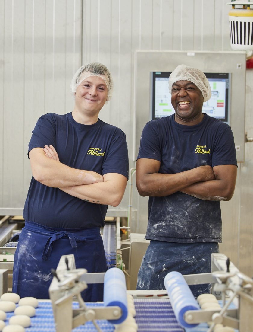 2 potige mannen die in een industriële bakkerij glimlachend hun werk doen