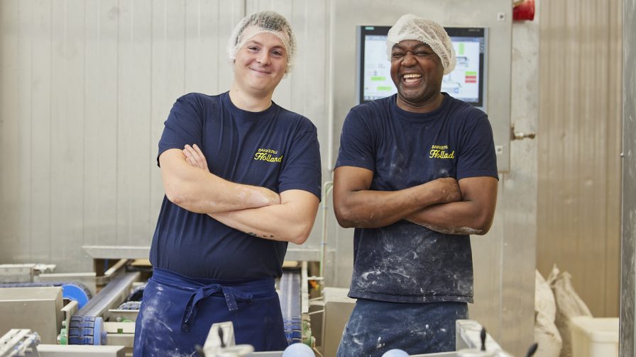 2 potige mannen die in een industriële bakkerij glimlachend hun werk doen