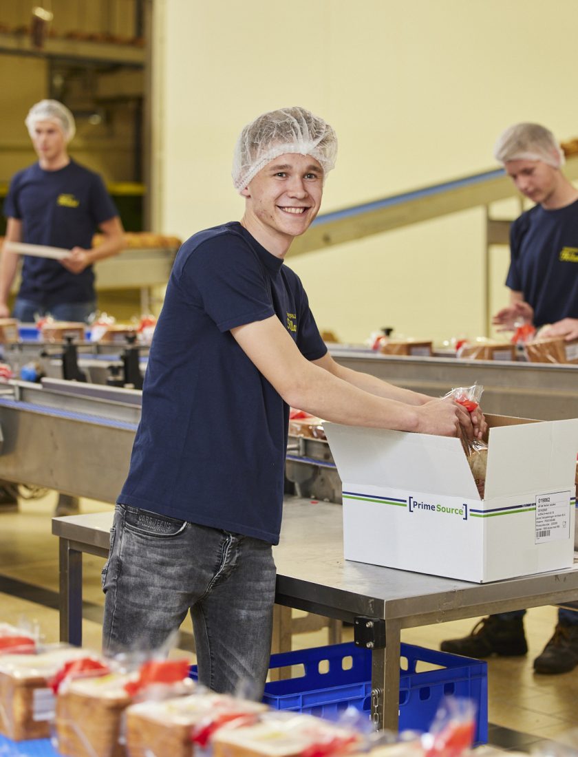 Productiemedewerkers binnen een industriële bakkerij broden aan het inpakken