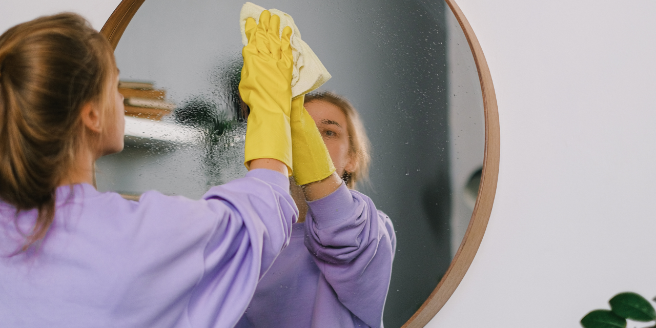 Vrouw maakt spiegel schoon met gele handschoenen aan