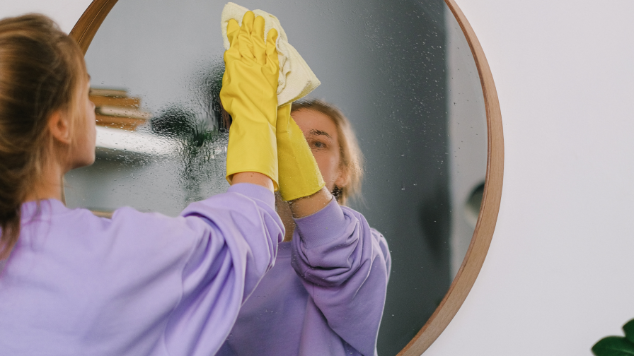 Vrouw maakt spiegel schoon met gele handschoenen aan