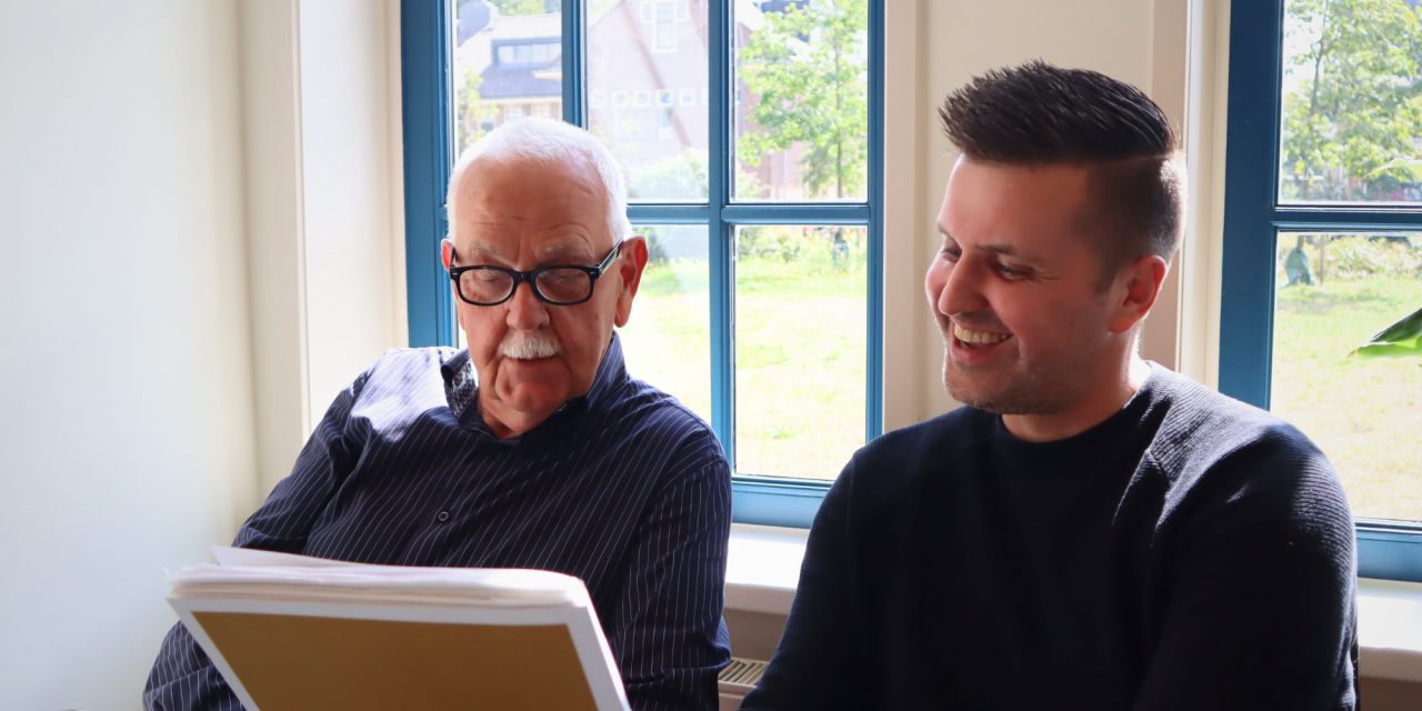 1 oudere man met bril en 1 man met donker haar die naar documenten kijken